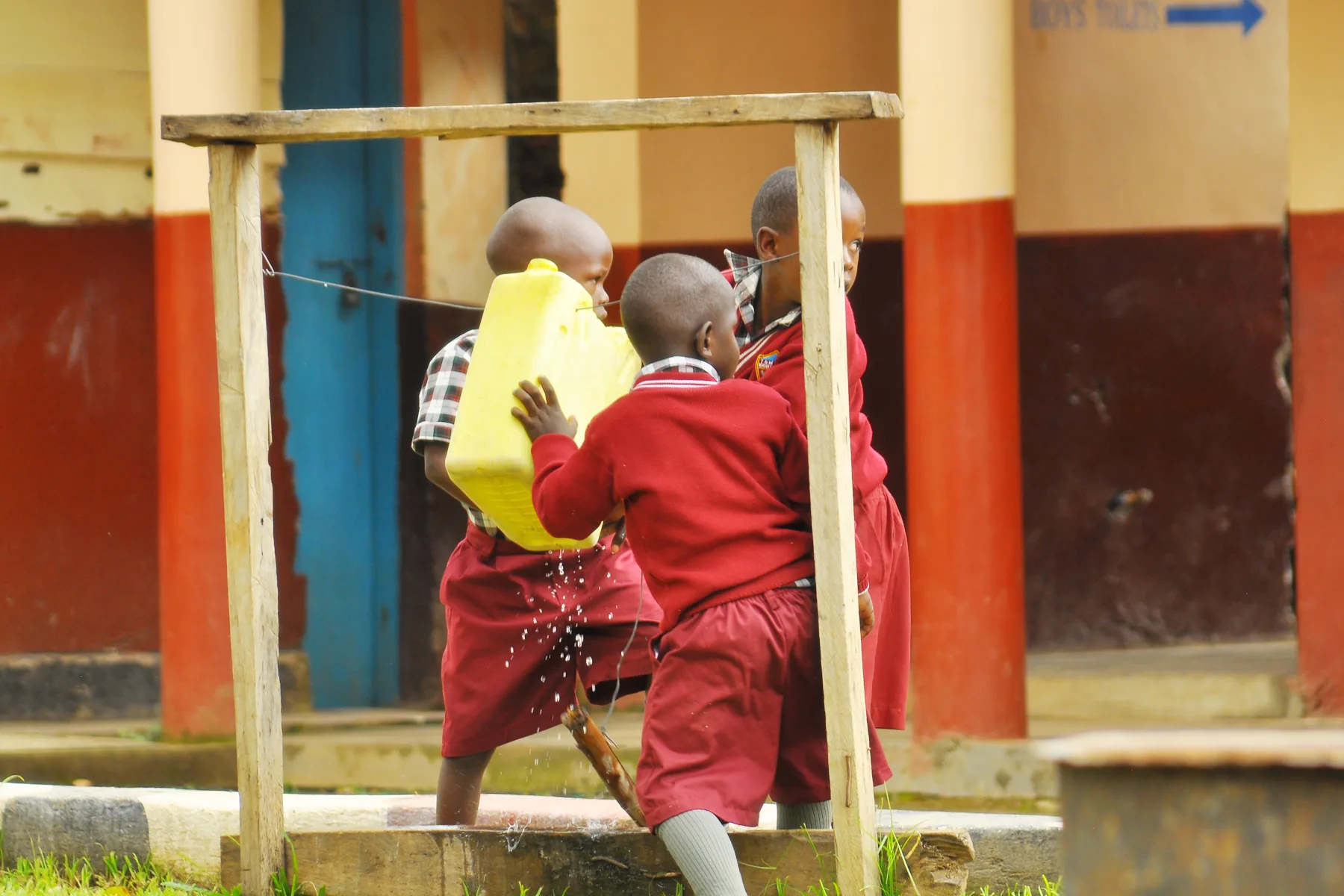 Young pupils carrying water together outside their classroom